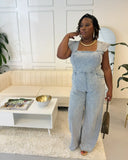 Plus size woman wearing a light blue denim jumpsuit with flutter sleeves, square neckline, and smocked back, styled for a casual-chic look