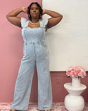 Plus size woman wearing a light blue denim jumpsuit with flutter sleeves, square neckline, and smocked back, styled for a casual-chic look