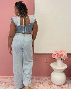 Plus size woman wearing a light blue denim jumpsuit with flutter sleeves, square neckline, and smocked back, styled for a casual-chic look